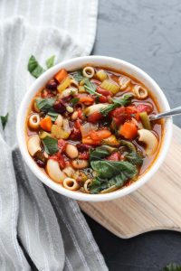 Big bowl of minestrone soup with fresh basil on top.