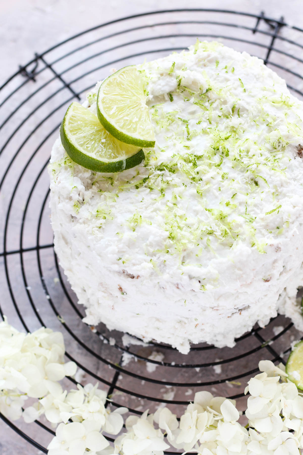 Frosted cake on metal rack with limes sliced on top.