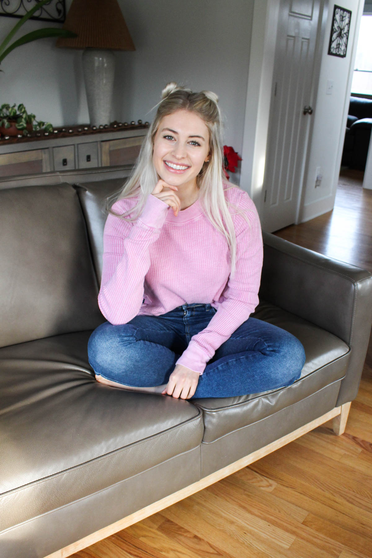 Girl sitting on couch with pink sweater and jeans.