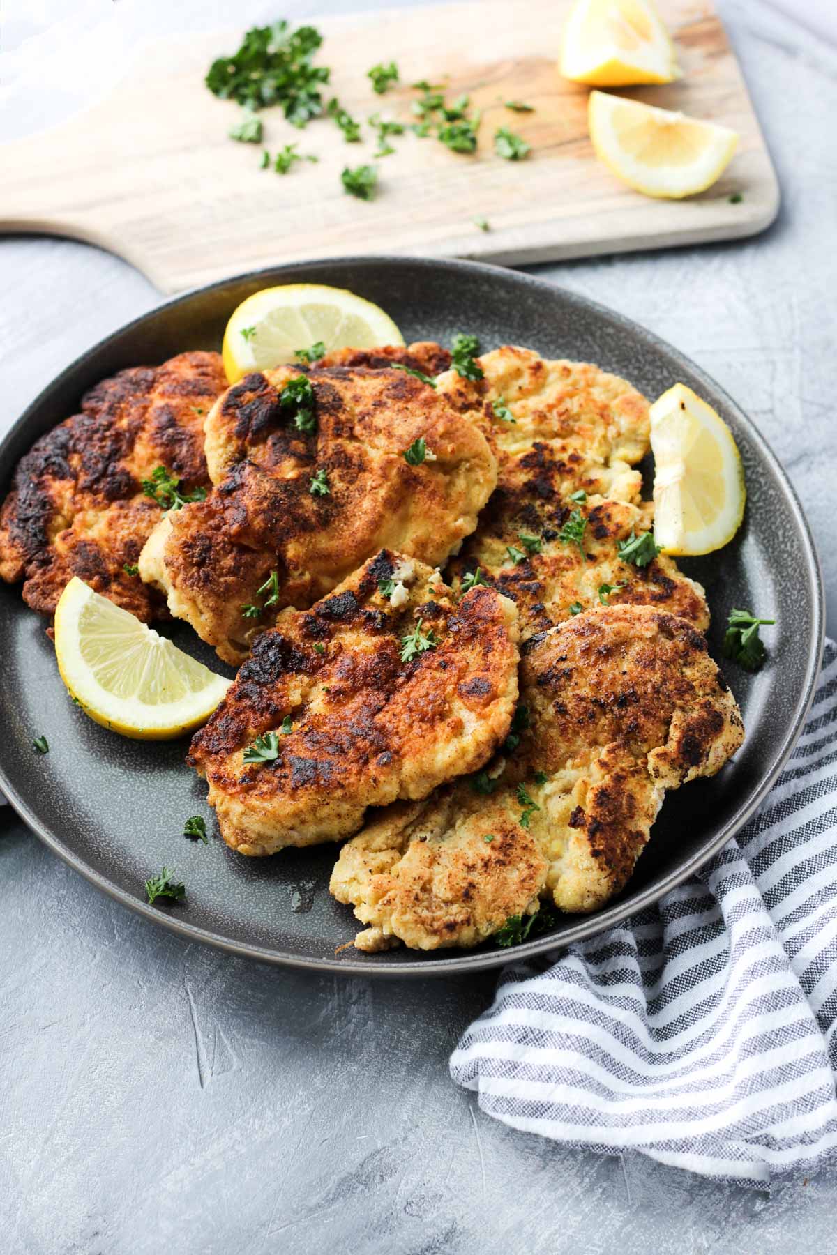 Plate of chicken cutlets with lemon slices and fresh parsley.