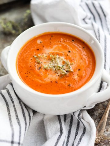 White bowl of tomato carrot soup with fresh thyme on top.