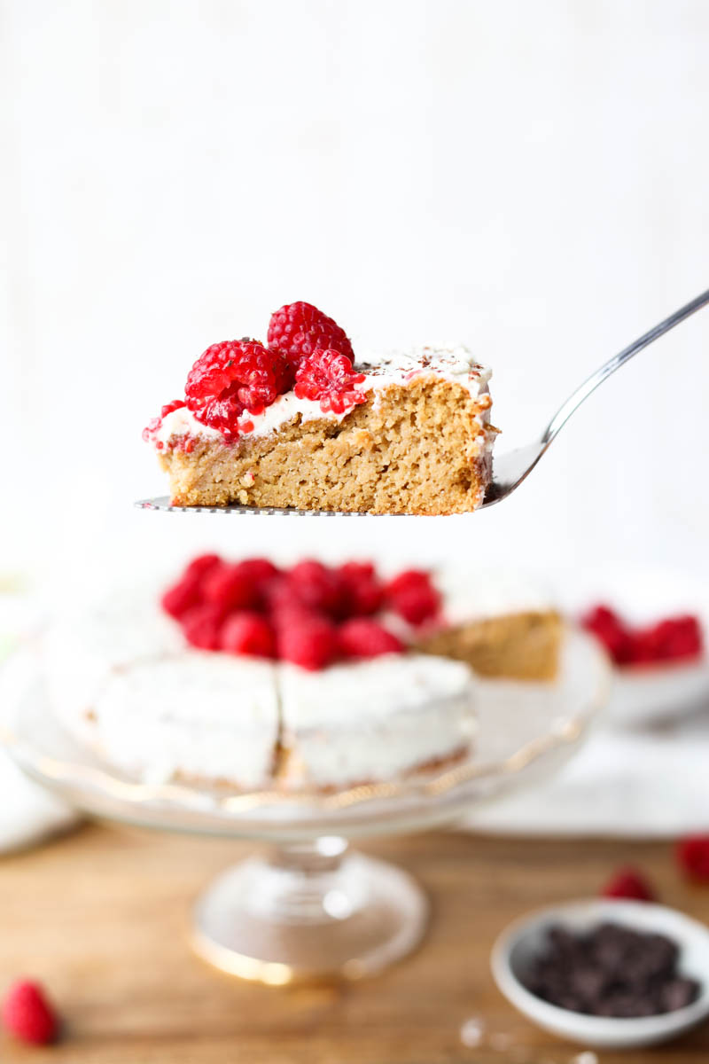 Holding up slice of vanilla cake with raspberries on top.