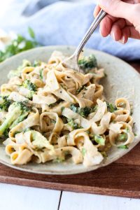Fork swirling pasta with chicken alfredo with broccoli.