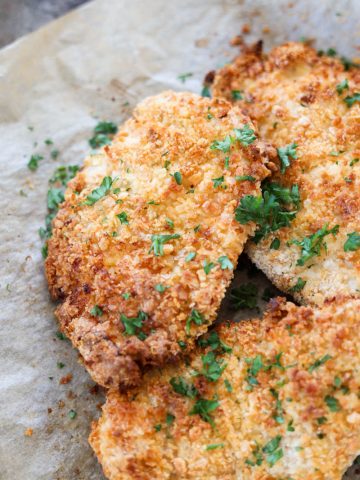 Close up picture of chicken cutlets with parsley on top.