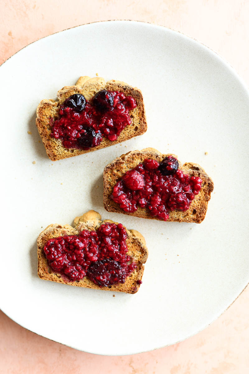 Three pieces of toast with berry jam on a white plate.