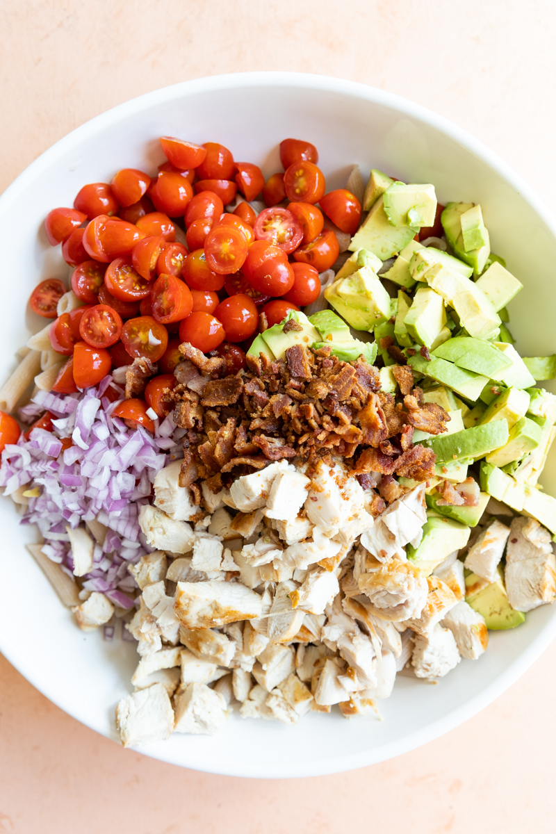 Pasta salad ingredients in a large white bowl.