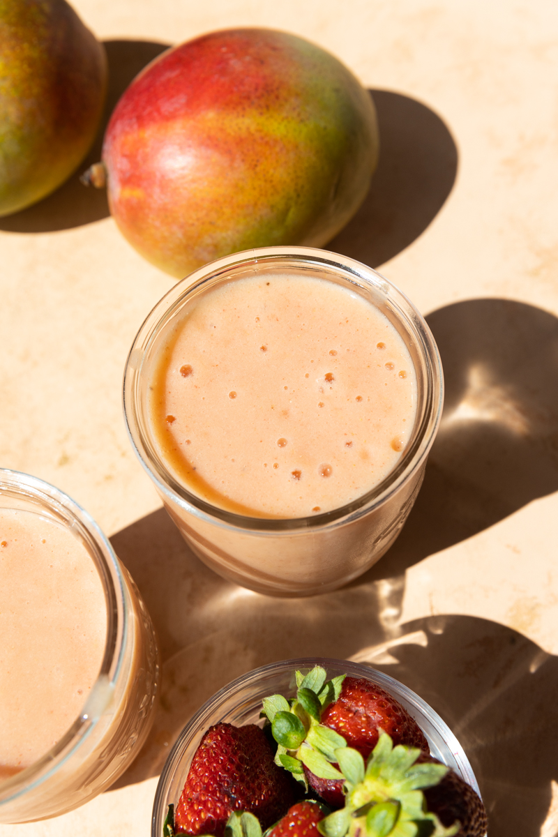 Overhead picture of smoothie in a glass cup with mango and strawberries.