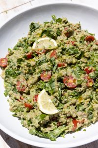 Pesto orzo salad in a white bowl with lemon slices on top.