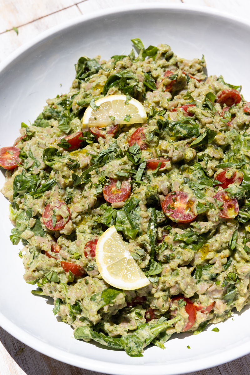 Pesto orzo salad in a white bowl with lemon slices on top.