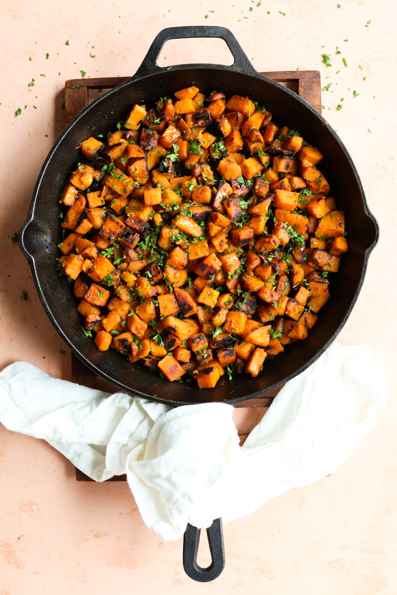 Sauteed sweet potato in a cast iron skillet sitting on a wooden cooling rack.