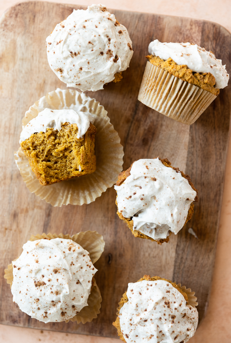 Pumpkin protein muffins on a wooden board with thick white frosting on top.