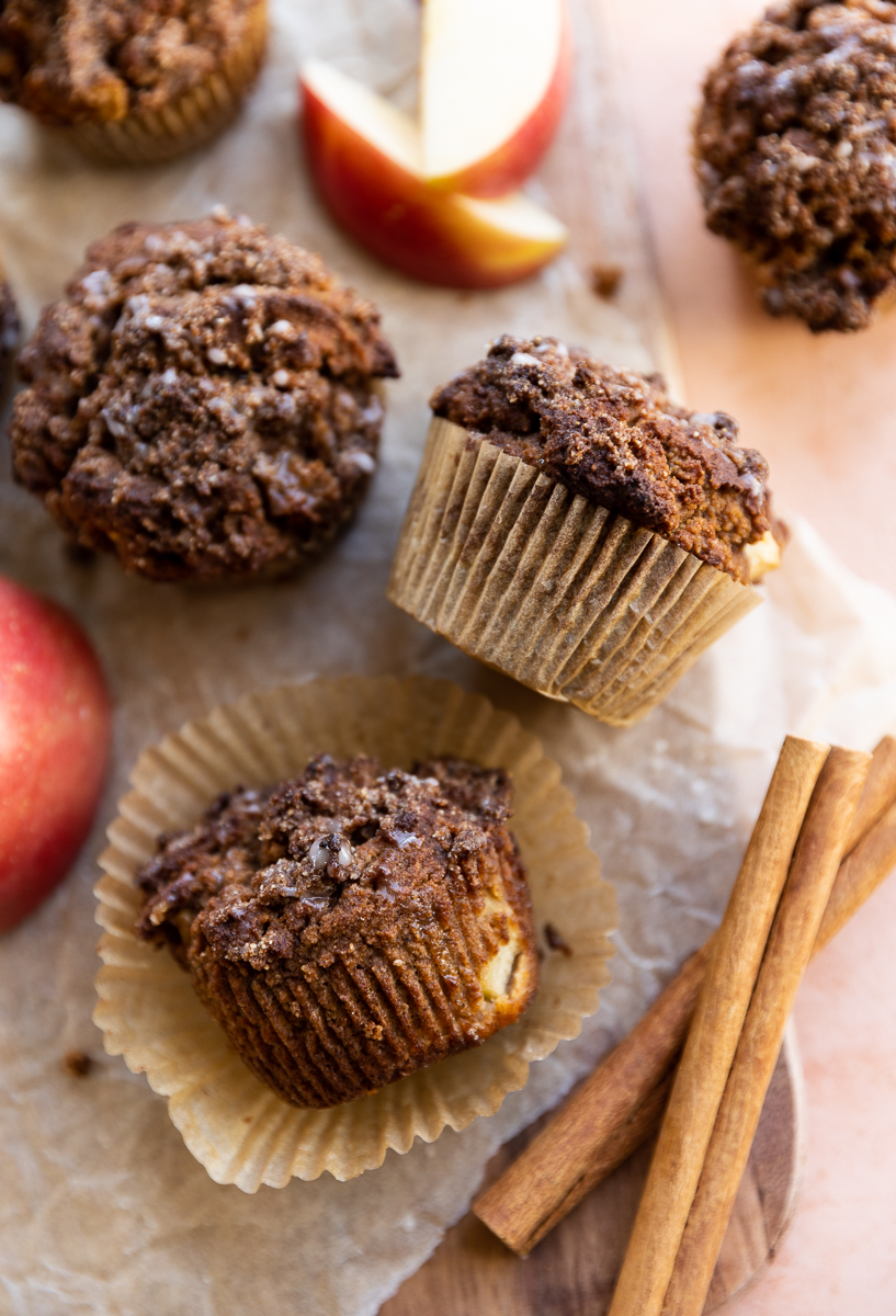 Apple crumble muffins on their side with cinnamon sticks and red apples.