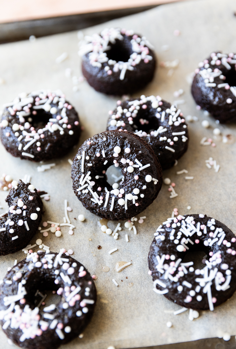 Mini chocolate donuts on parchment paper lined baking sheet.