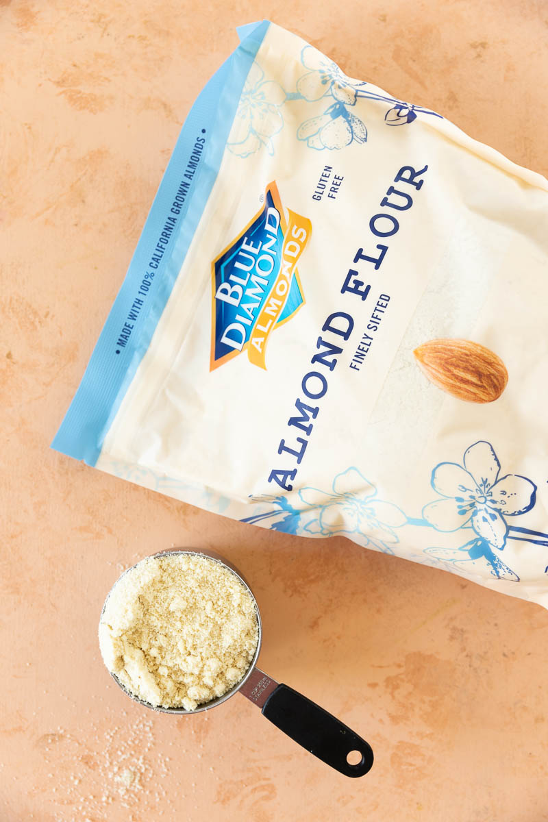 A bag of blue diamond almond flour next to a measuring cup filled with almond flour.