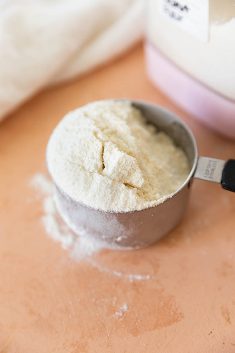 Coconut flour in a measuring cup with some flour spilling down the side.