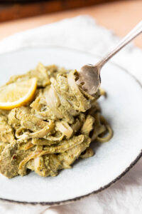 Close up picture of fork twirling creamy pesto pasta with artichoke hearts and lemon.