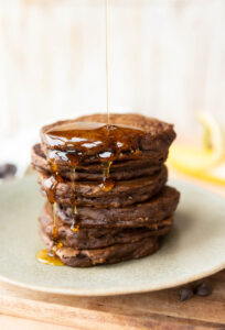 Big stack of chocolate protein pancakes with syrup dripping down the side.