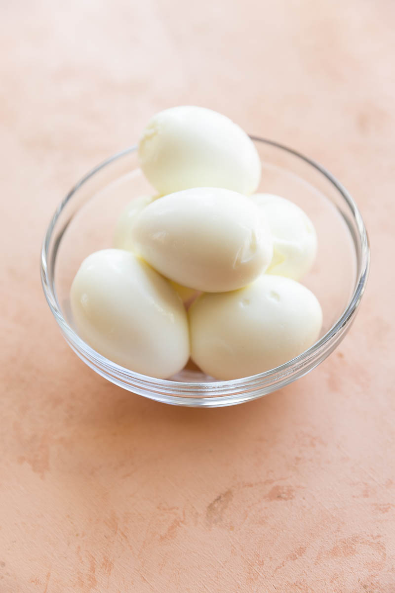 Peeled hard boiled eggs in a glass bowl.