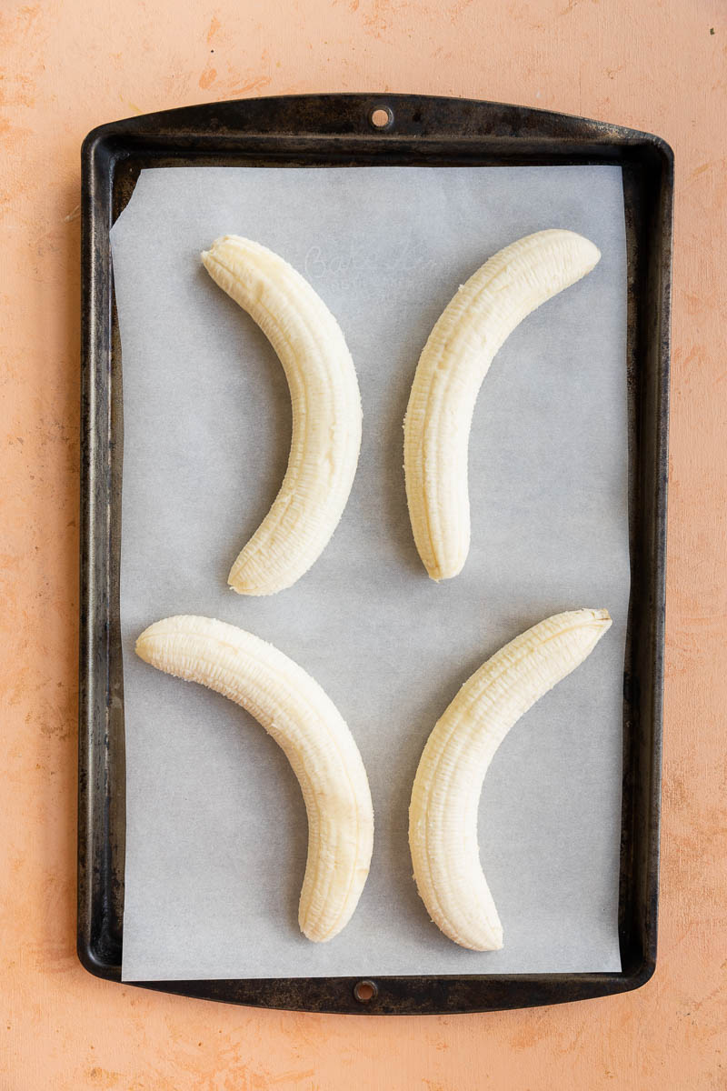 Whole peeled bananas on a baking sheet lined with parchment paper.