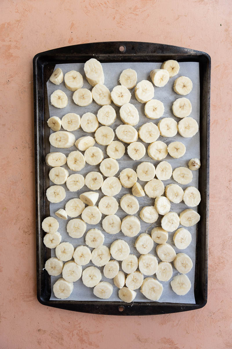 Banana discs spread out on a baking sheet lined with parchment paper.