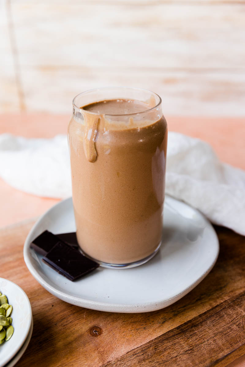 Chocolate banana protein shake with chocolate chunks next to the glass cup.
