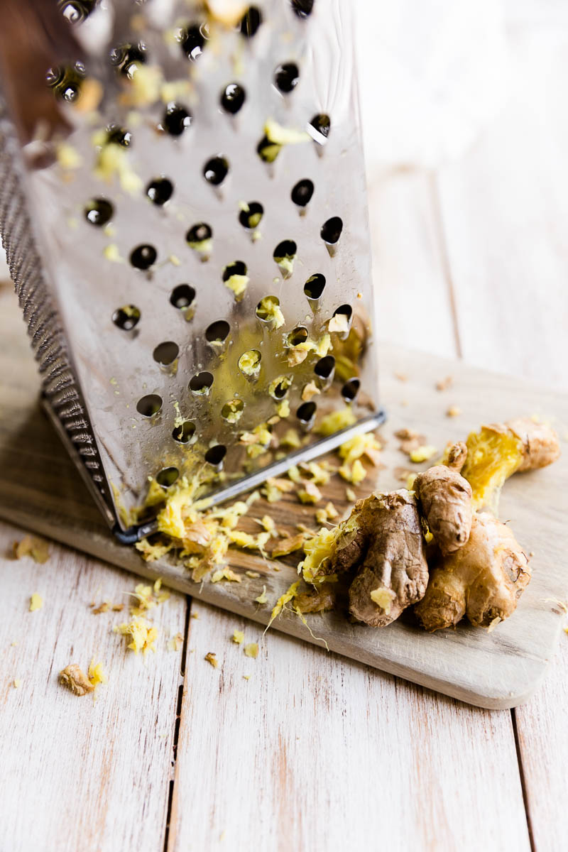 Grater with grated ginger on a cutting board.