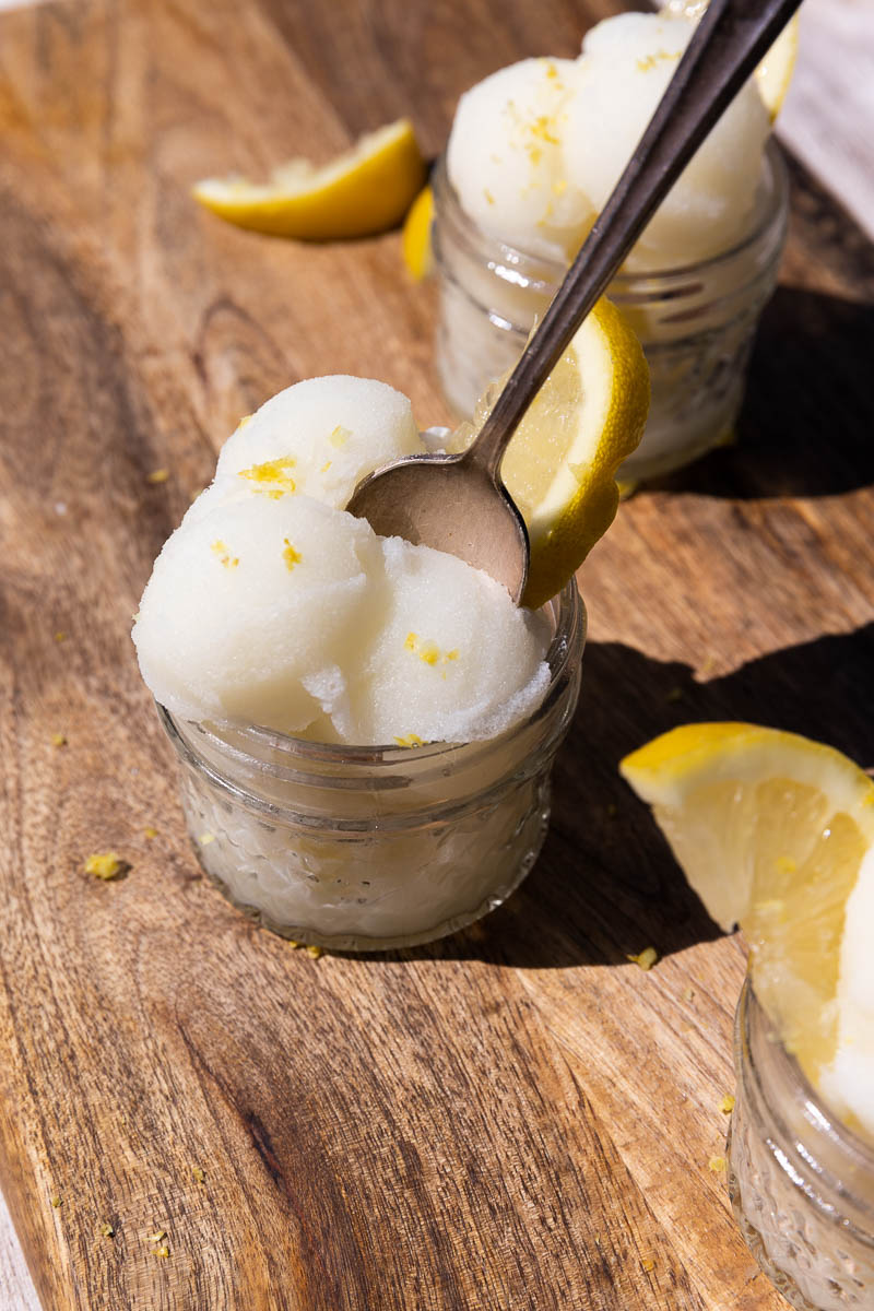 Spoon sticking out of lemon sorbet in a glass cup.