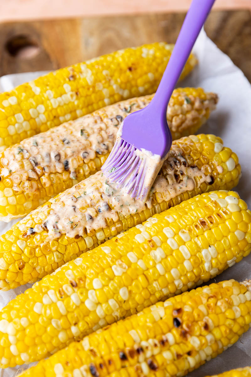 Brushing creamy sauce onto the grilled corn.