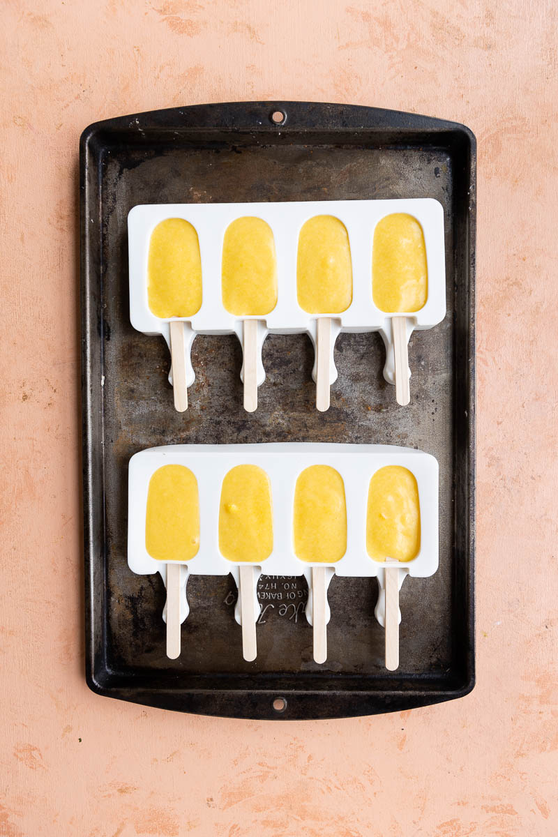Popsicle molds filled with orange protein mixture.