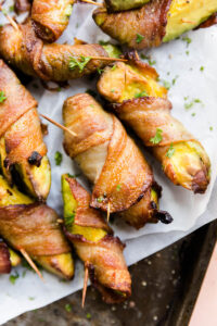 Bacon wrapped avocado on a parchment paper lined baking sheet.