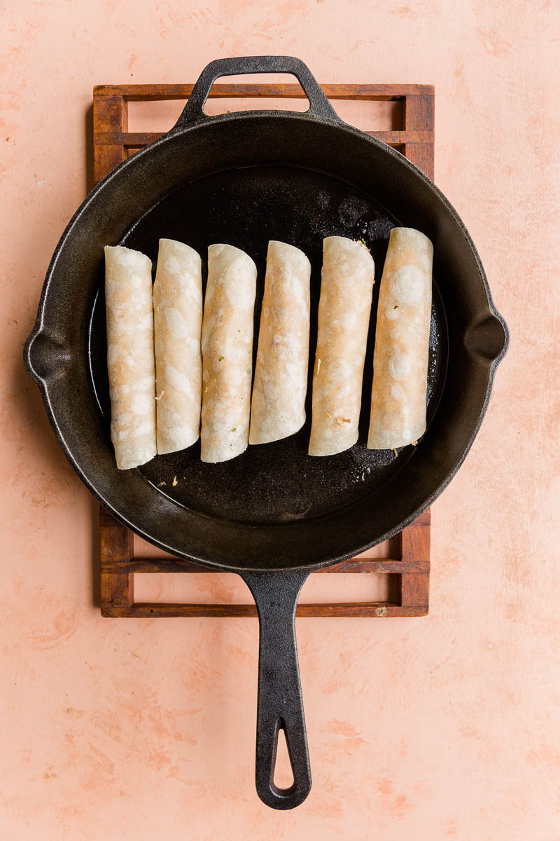 Taquitos cooking in a cast iron skillet.