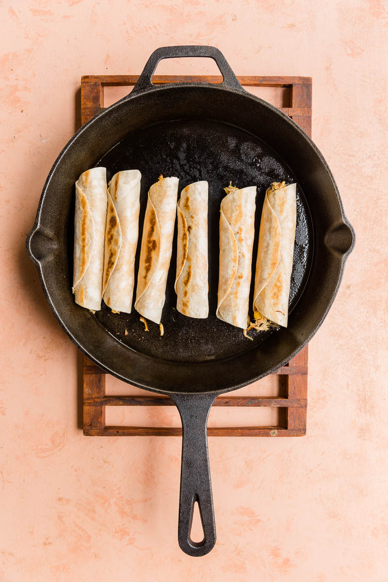 Cooked taquitos in a cast iron skillet.