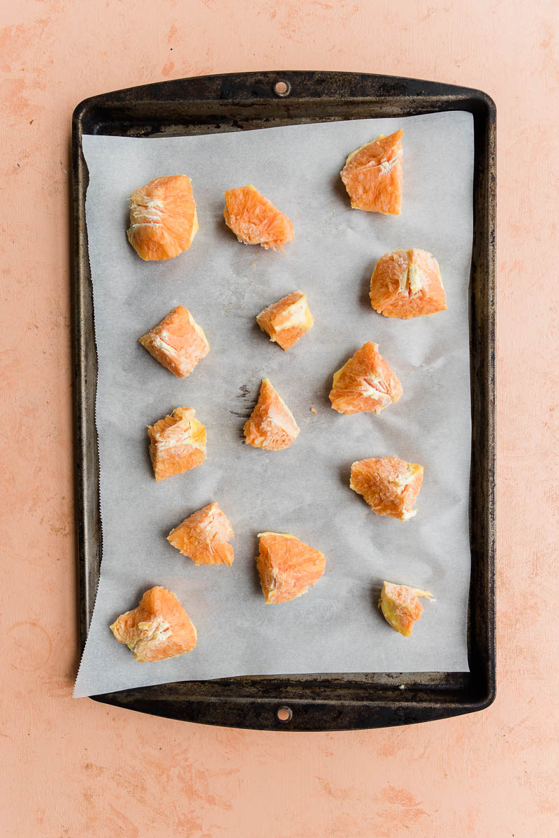Frozen orange chunks on a parchment paper lined baking sheet.