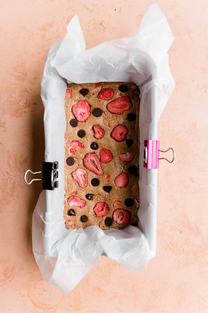 Strawberry protein bar mixture pressed into a parchment paper lined bread pan.