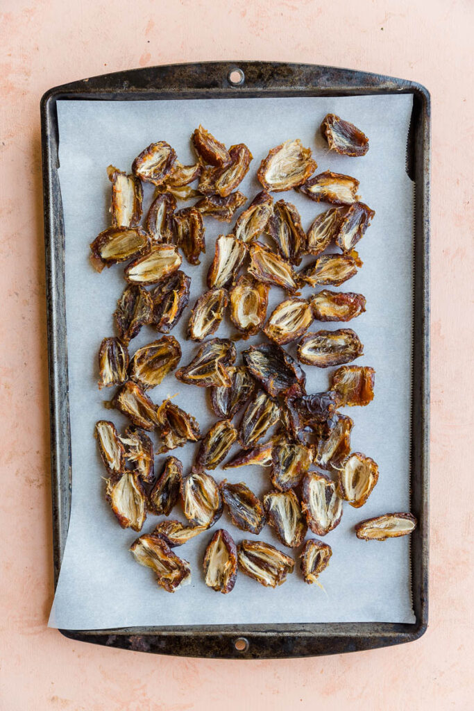 Pitted dates cut in half and spread out on a parchment paper lined baking sheet.