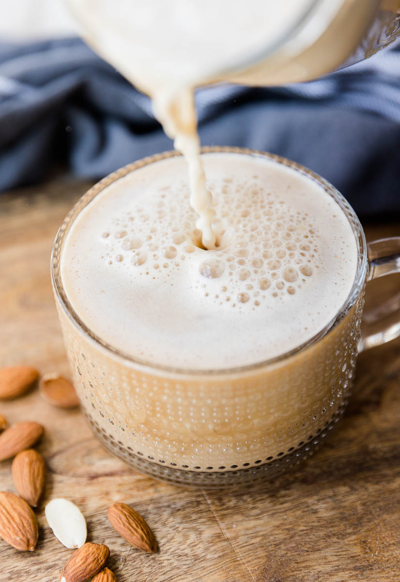 Homemade almond milk being poured into glass coffee mug.