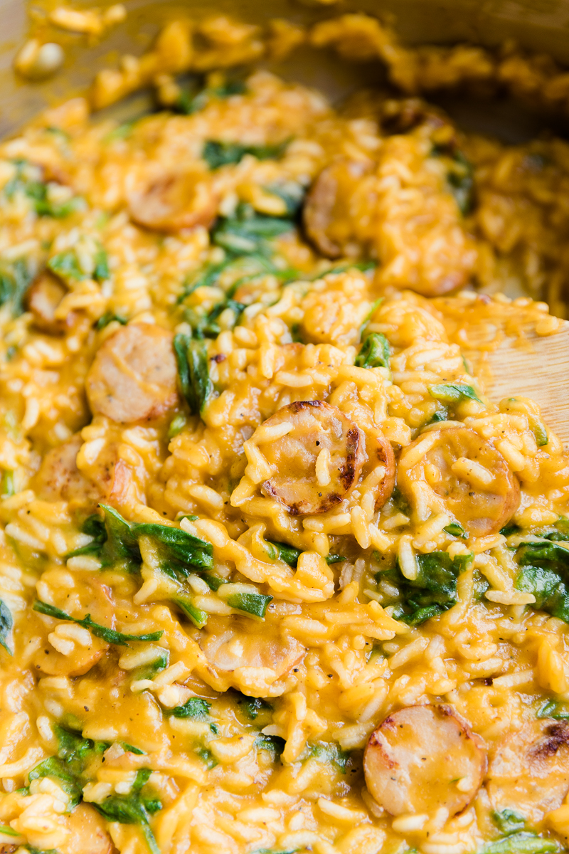 Close up picture of creamy chicken sausage and rice with spinach in large pan.