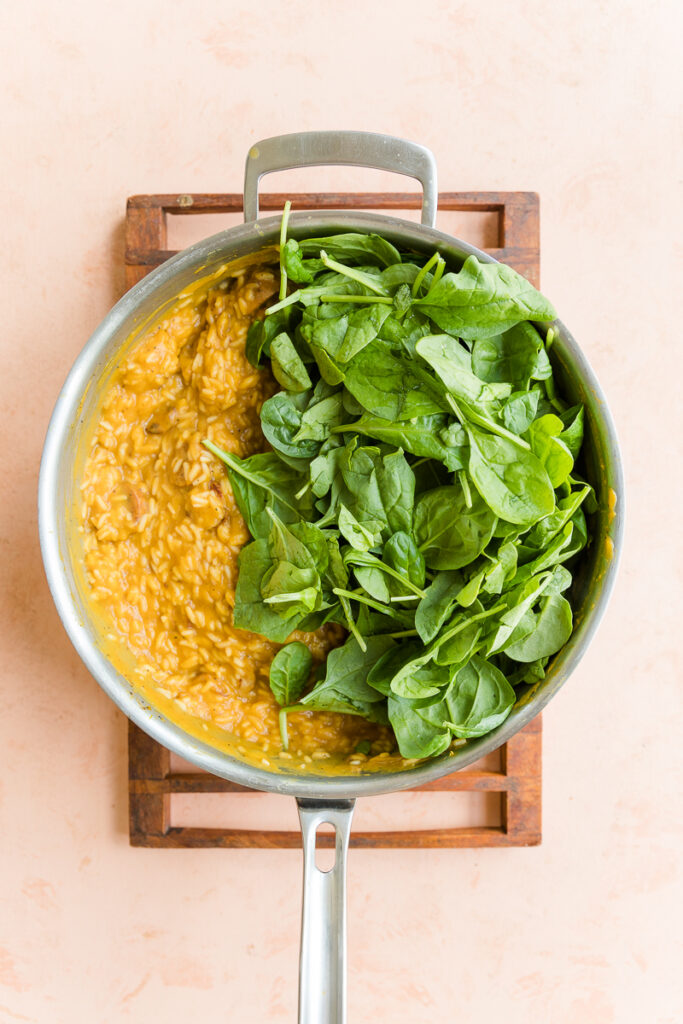 Cooked rice in creamy sauce with fresh spinach on top.