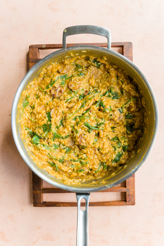 Creamy chicken sausage and rice in a large pot with spinach.