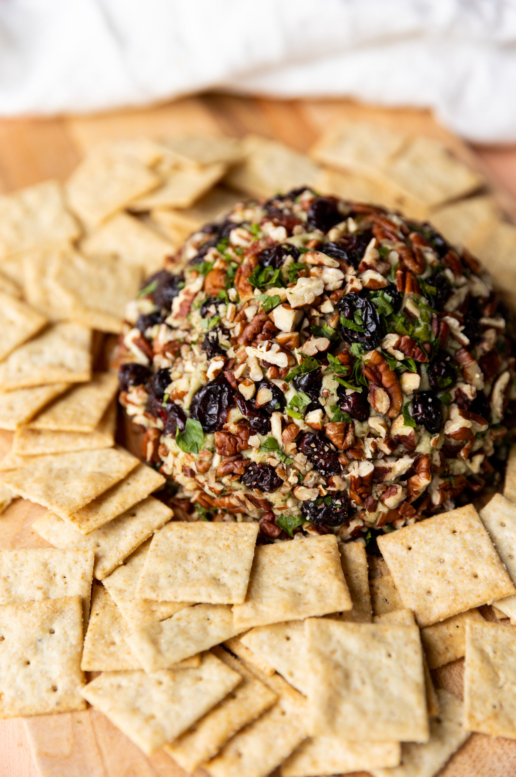 Vegan cheese ball covered in dried cranberries, pecans, and fresh parsley.