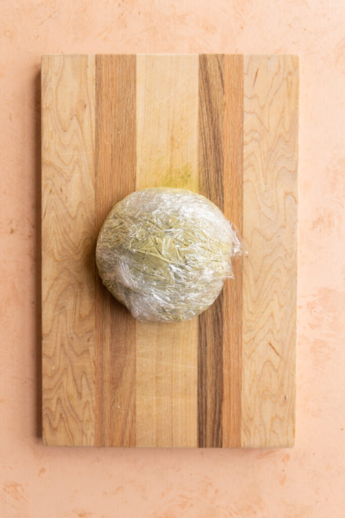 Cheese ball shaped on wood board and covered in plastic wrap.