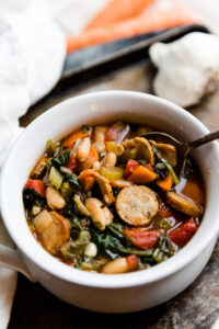 Spoon scooping out chicken sausage soup out of a white ceramic bowl.