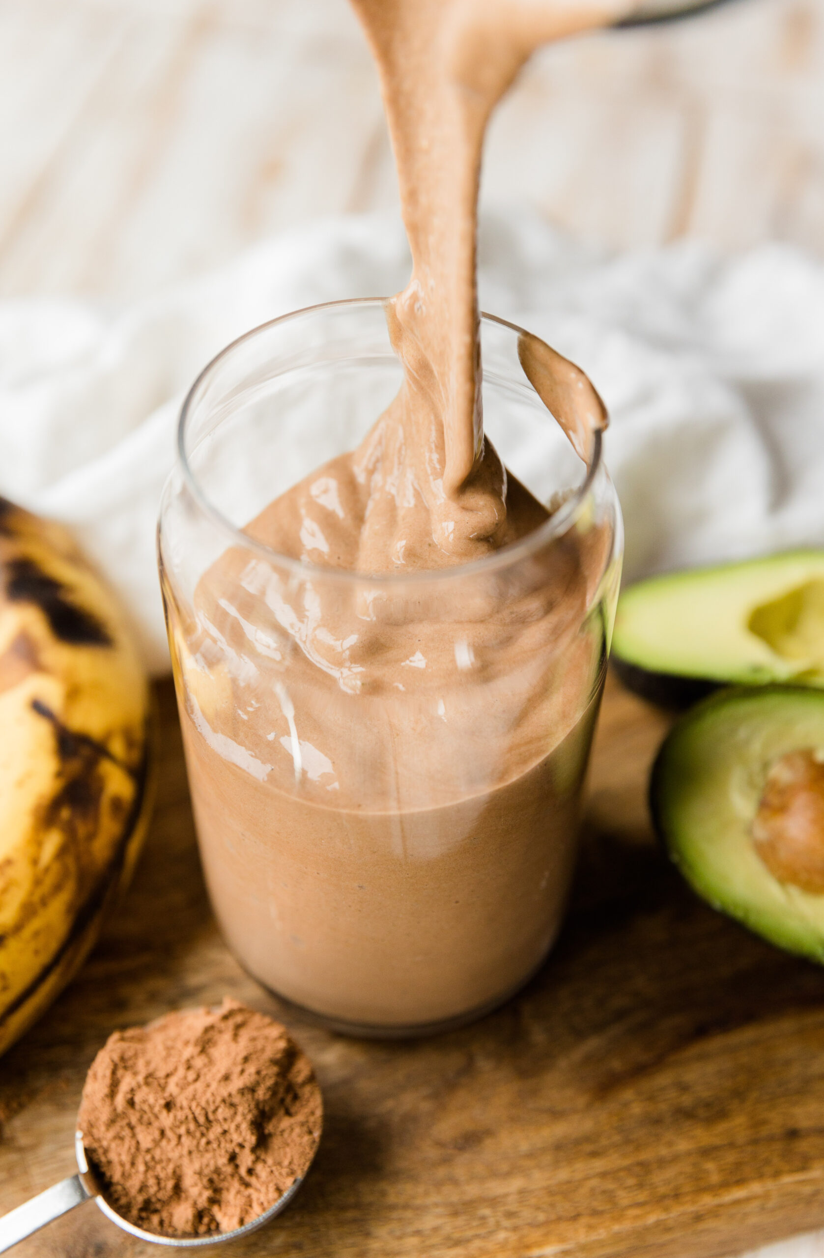 Thick chocolate protein shake being poured into glass cup.