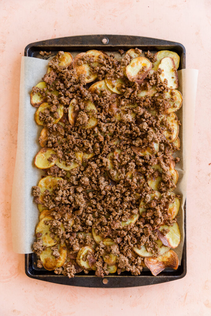 Crispy potato discs layered on a sheet pan with cooked ground beef on top.