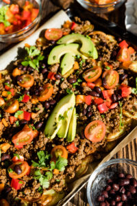 Potato nachos with tomato, bell peppers, black beans, and avocado on top.