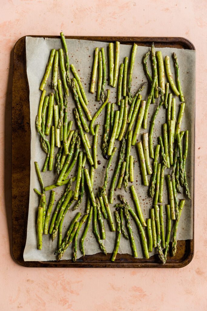 Marinated balsamic asparagus on a baking sheet with parchment paper.