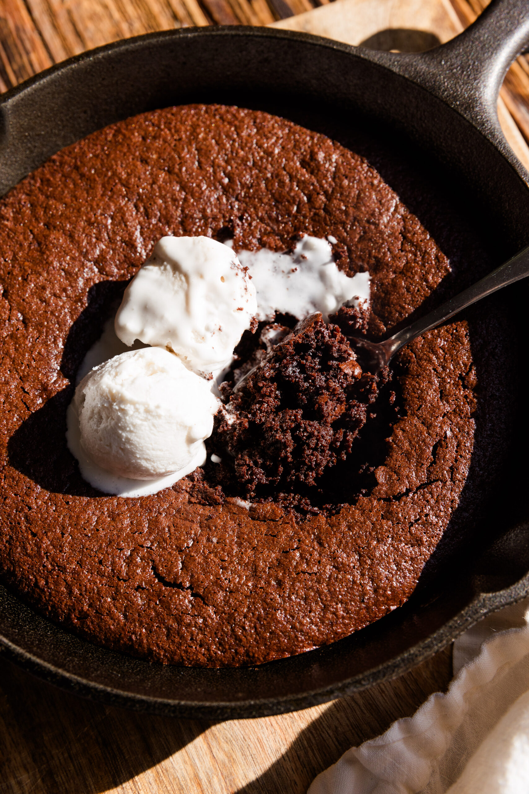 Gooey brownie skillet with spoon scooping out a big bite with coconut whipped cream on top.
