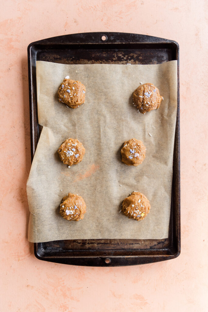 Funfetti cookie dough balls on a parchment paper lined baking sheet.