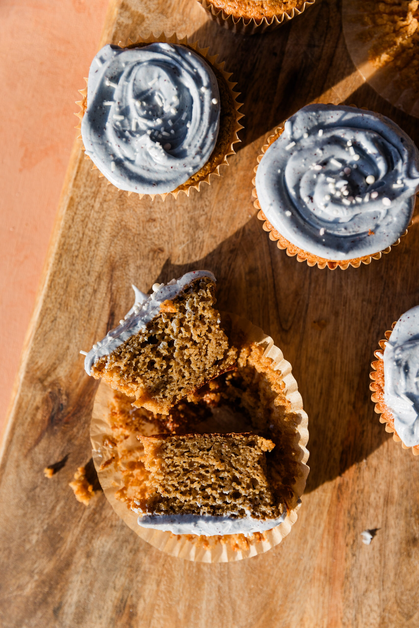 Gluten free vanilla cupcake cut in half with blue frosting on a wood board.