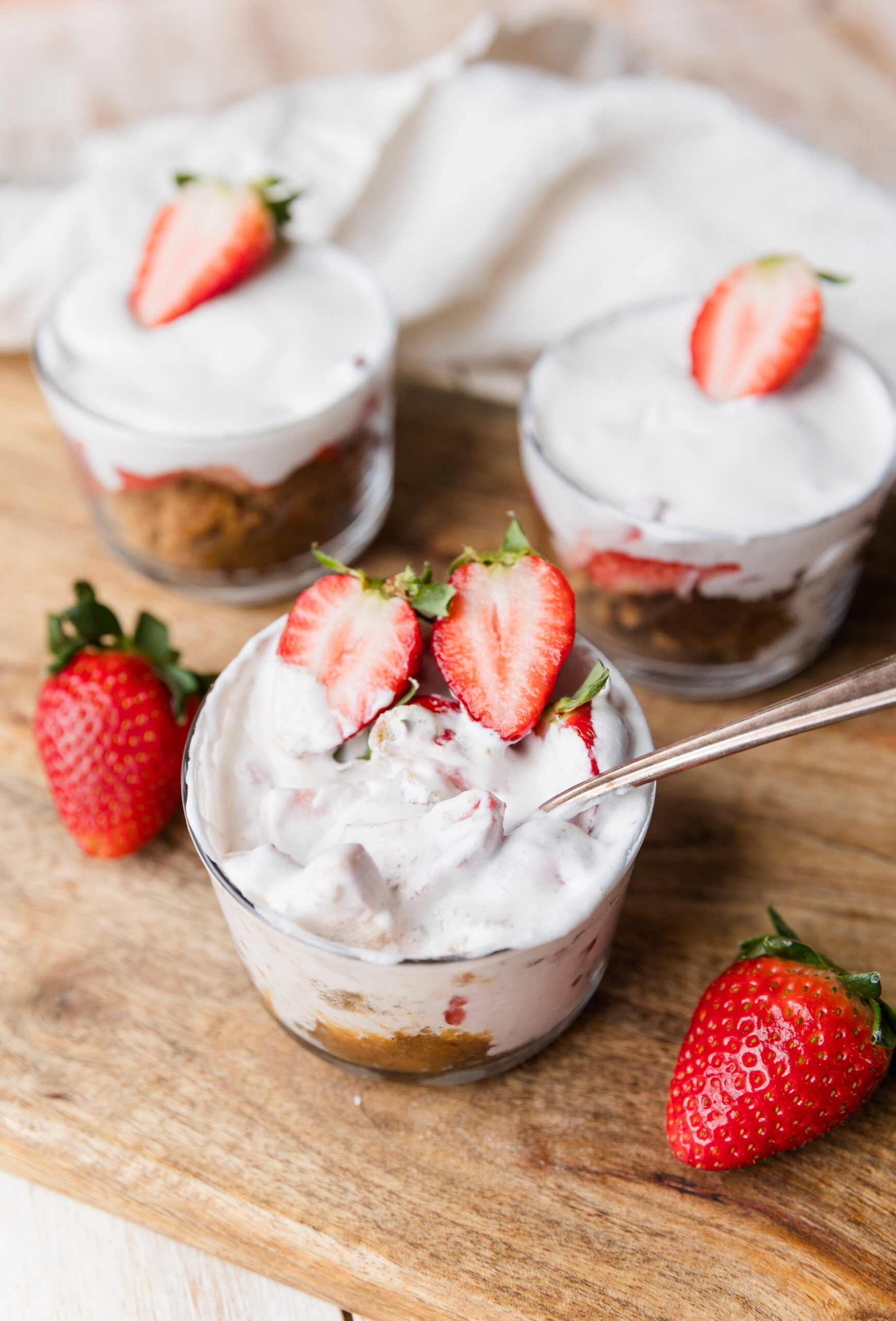 Strawberry shortcake cups with fresh strawberries on top with a spoon ready to take a bite.